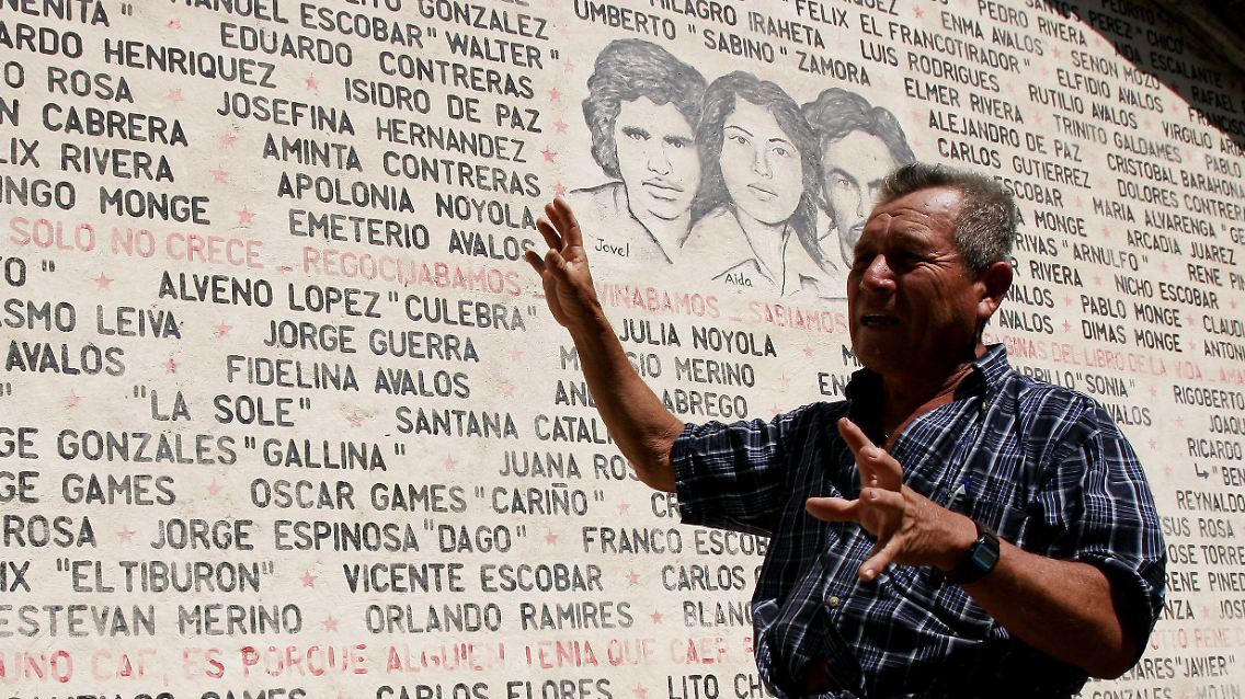 Historiker Pablo Alvarenga, der die Guerilla einst logistisch unterstützte, vor einer Tafel mit den Namen der ortsansässigen Opfer des Bügerkriegs in El Salvador.