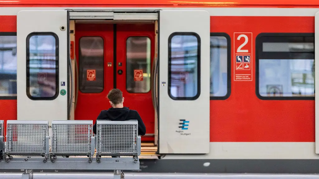Ein-Mann-sitzt-an-einem-Bahnhof-vor-einem-Regionalzug-auf-der-Bank