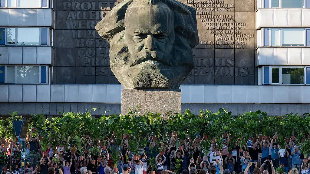 Teilnehmer-einer-Kunstperformance-halten-in-der-Innenstadt-von-Chemnitz-Zimmerpflanzen-vor-dem-Karl-Marx-Monument-dem-Wahrzeichen-der-Stadt-in-die-Hoehe