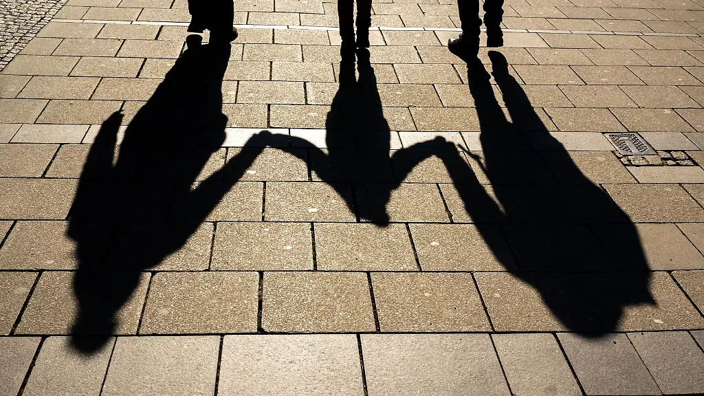 Die-Schatten-von-zwei-Erwachsenen-und-einem-Kind-fallen-in-den-Morgenstunden-auf-den-Asphalt