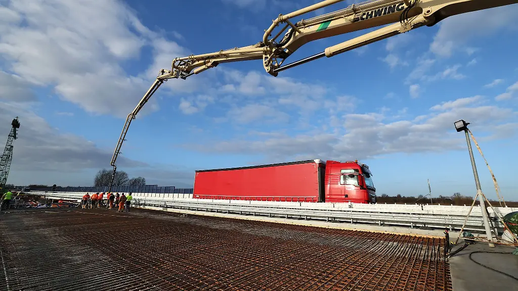 Ein-weiteres-Stueck-der-neuen-Bruecke-der-Ostseeautobahn-A20-im-Trebeltal-wird-mit-einem-Betonlift-betoniert-im-Hintergrund-rollt-der-Verkehr-auf-der-fertigen-Richtungsfahrbahn