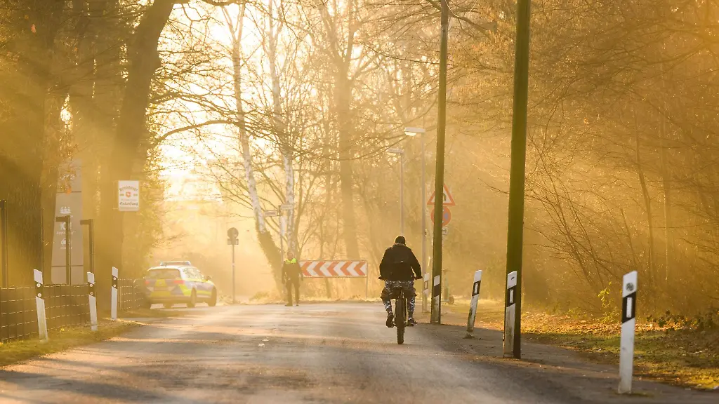 Ein-Mann-faehrt-mit-einem-Fahrrad-ueber-eine-Strasse-waehrend-die-aufgehende-Sonne-den-morgendlichen-Fruehnebel-in-goldenes-Licht-taucht