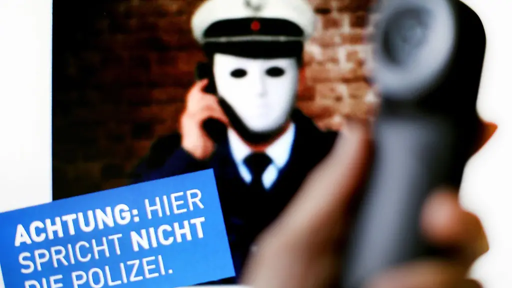 Ein-Telefonhoerer-wird-vor-ein-Plakat-der-Polizei-mit-der-Aufschrift-Achtung-Hier-spricht-NICHT-die-Polizei-gehalten