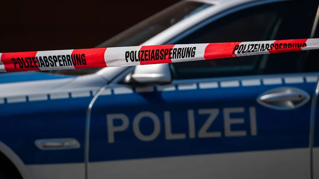 Ein-Polizeiauto-steht-hinter-einem-Absperrband-der-Polizei