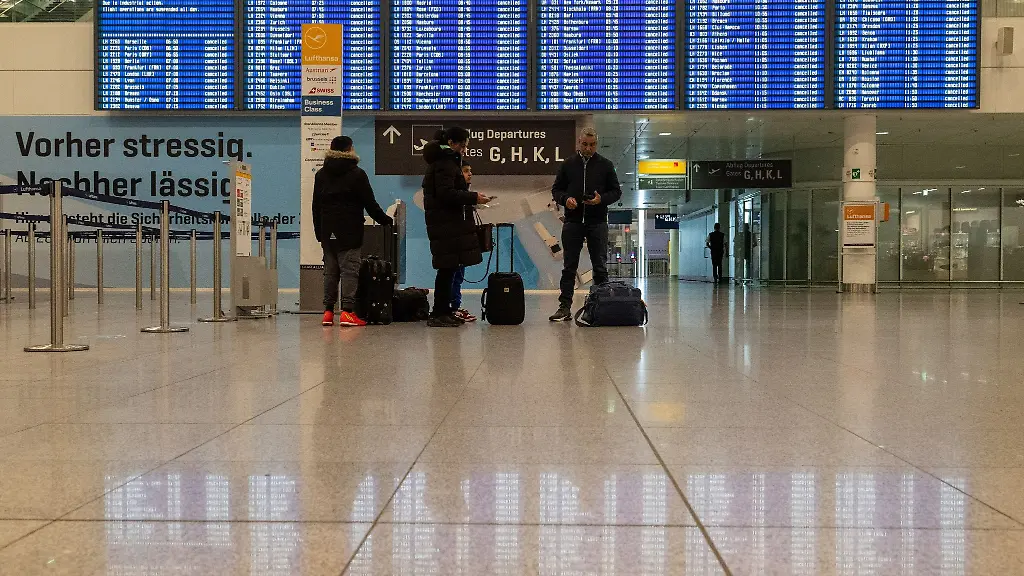 Gestrandete-Passagiere-stehen-am-Flughafen-Muenchen-vor-einer-Anzeigetafel