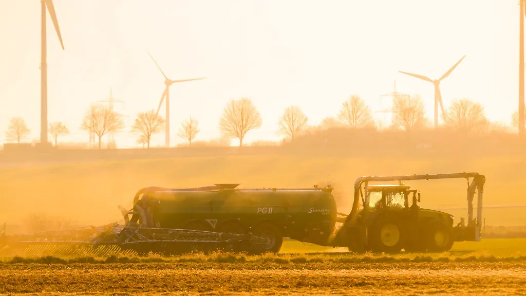 Mit-einem-Traktor-wird-bei-Sonnenaufgang-ein-Feld-mit-Guelle-geduengt