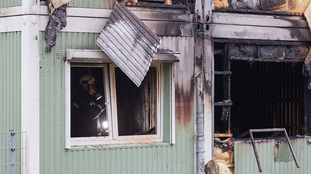 Ein-Feuerwehrmann-steht-mit-einer-Lampe-in-einem-zerstoerten-Containerhaus-der-Gefluechtetenunterkunft