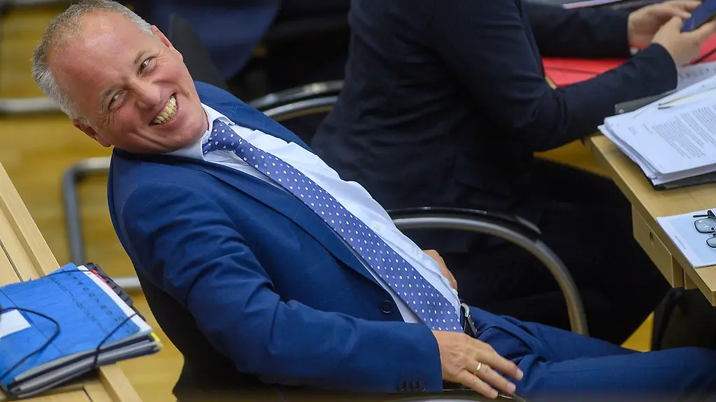 Ruediger-Erben-sitzt-im-Plenarsaal-an-seinem-Platz-und-lacht