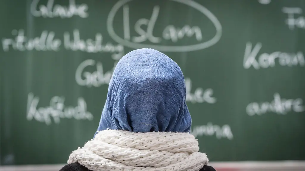 Eine-junge-Frau-mit-Kopftuch-sitzt-in-einer-Schule-vor-einer-Tafel