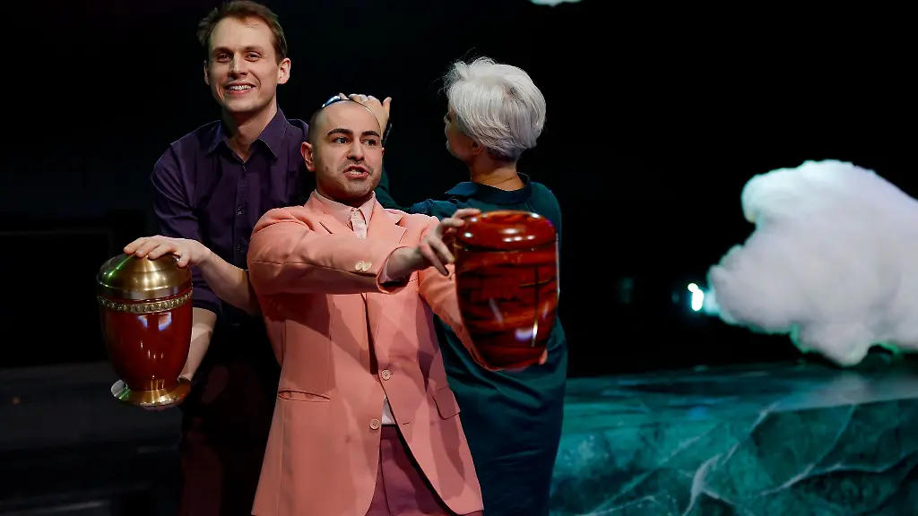 Yascha-Finn-Nolting-l-r-Aydin-Aydin-und-Adeline-Schebesch-preisen-verschiedene-Urnen-an-in-dieser-Szene-des-Theaterstuecks-Exit-Sterben-fuer-Anfaenger-innen-im-Staatstheater-Nuernberg