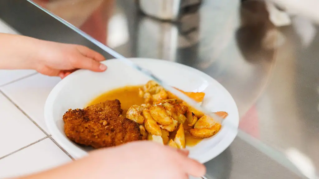 Eine-Grundschuelerin-nimmt-einen-Teller-mit-Schnitzel-Kartoffeln-und-Sosse-vom-Tresen-der-Essensausgabe-einer-Schulmensa