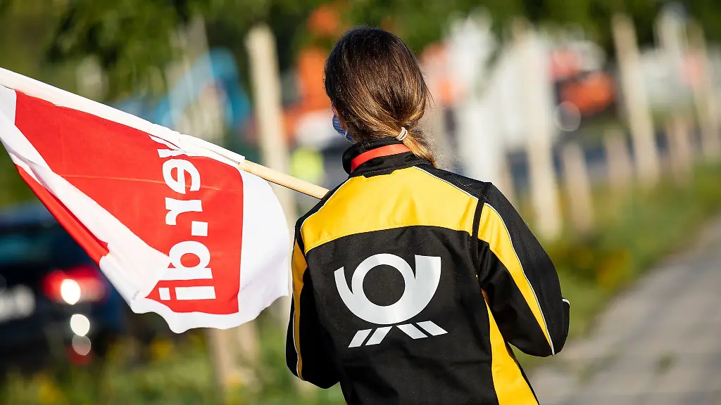 Eine-Beschaeftigte-der-Deutschen-Post-steht-mit-einer-Fahne-der-Gewerkschaft-Verdi-vor-einer-Deutsche-Post-DHL-Niederlassung