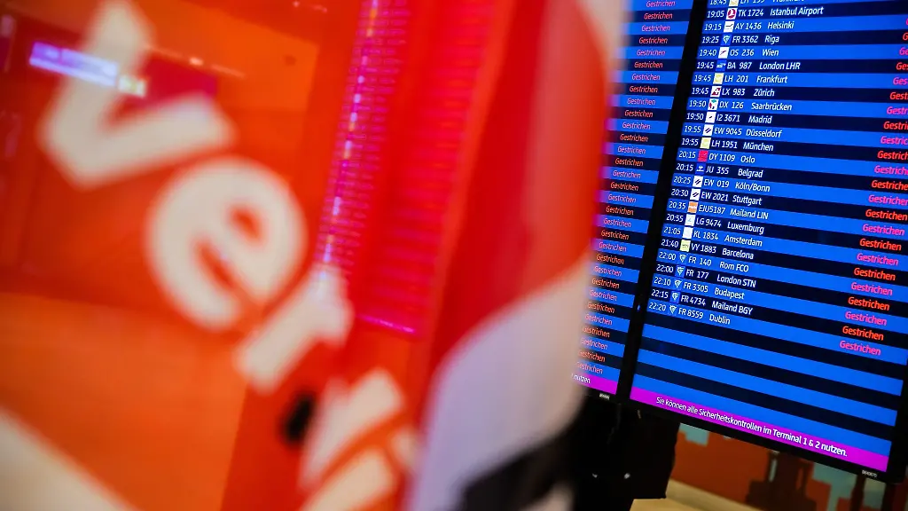 Eine-Verdi-Fahne-ist-waehrend-eines-Warnstreiks-am-Flughafen-Berlin-Brandenburg-BER-vor-einer-Anzeigetafel-zu-sehen