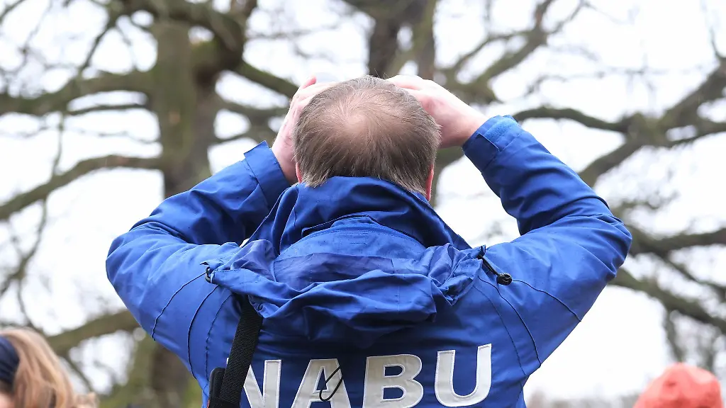 Ein-Mann-mit-einer-Jacke-des-Naturschutzbunds-Deutschland-NABU-blickt-durch-ein-Fernglas