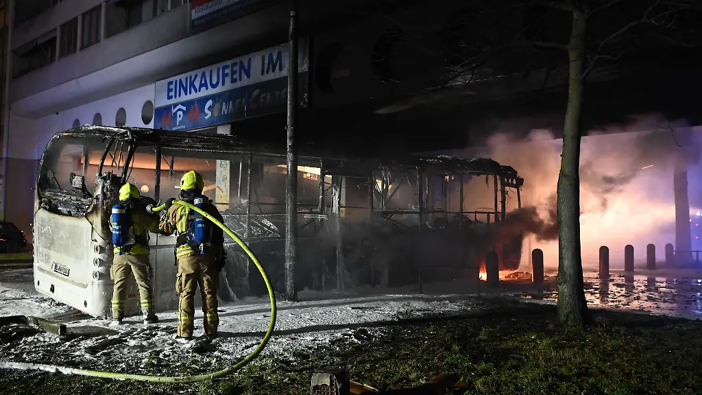 Einsatzkraefte-der-Feuerwehr-loeschen-in-der-Silvesternacht-an-der-Sonnenallee-im-Bezirk-Neukoelln-einen-brennenden-Bus-der-von-Unbekannten-angezuendet-worden-war