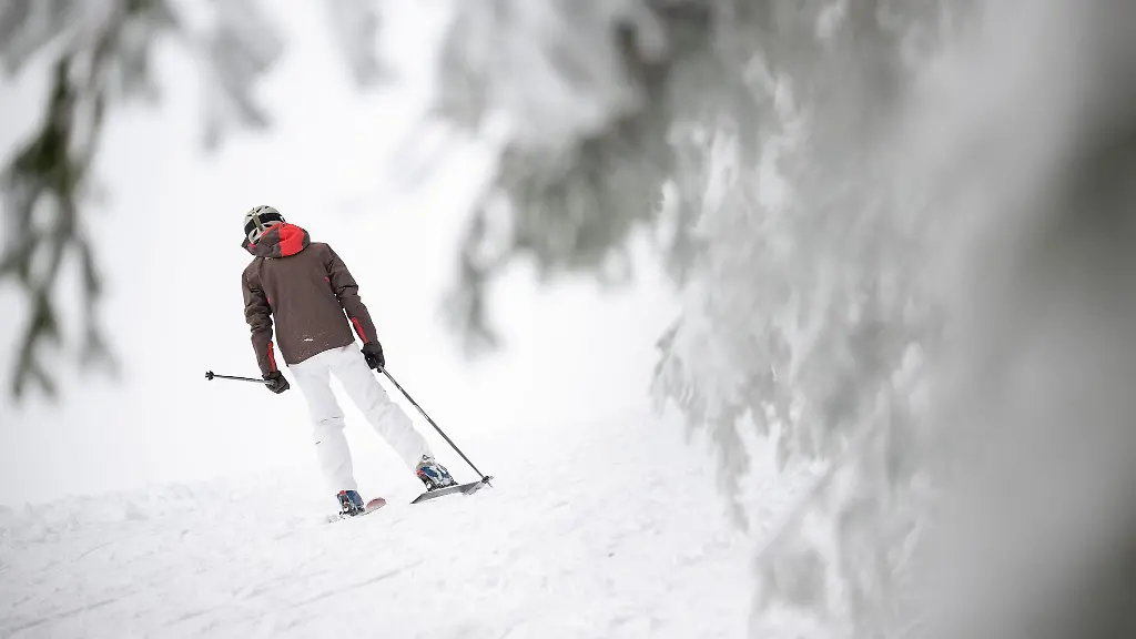 Ein-Skifahrer-faehrt-auf-der-Wasserkuppe-an-verschneiten-Baeumen-vorbei