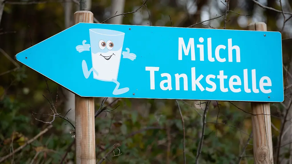 Ein-Schild-weist-den-Weg-zu-einer-Milchtankstelle-einem-gekuehlten-Verkaufsautomaten-fuer-Rohmilch-ab-Hof
