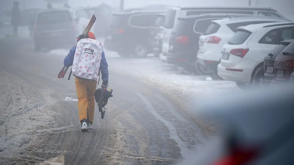 Ein-Skifahrer-geht-mit-Skiern-ueber-einen-vollen-Parkplatz