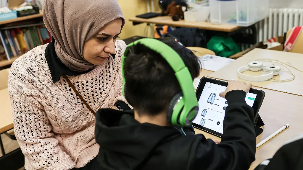 Eine-Lehrerin-betreut-in-einer-Grundschulklasse-einen-Schueler-der-am-iPad-lernt