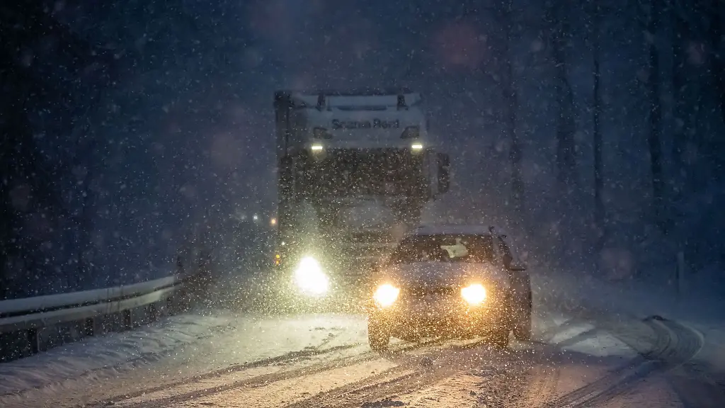 Ein-Auto-ueberholt-einen-Lastwagen-der-auf-der-schneebedeckten-Fahrbahn-an-einer-Steigung-liegen-geblieben-ist