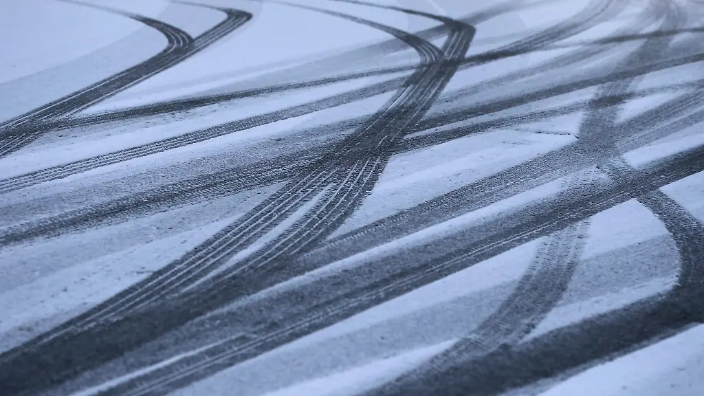Reifenspuren-zeichnen-sich-auf-einer-Strasse-im-Schnee-ab