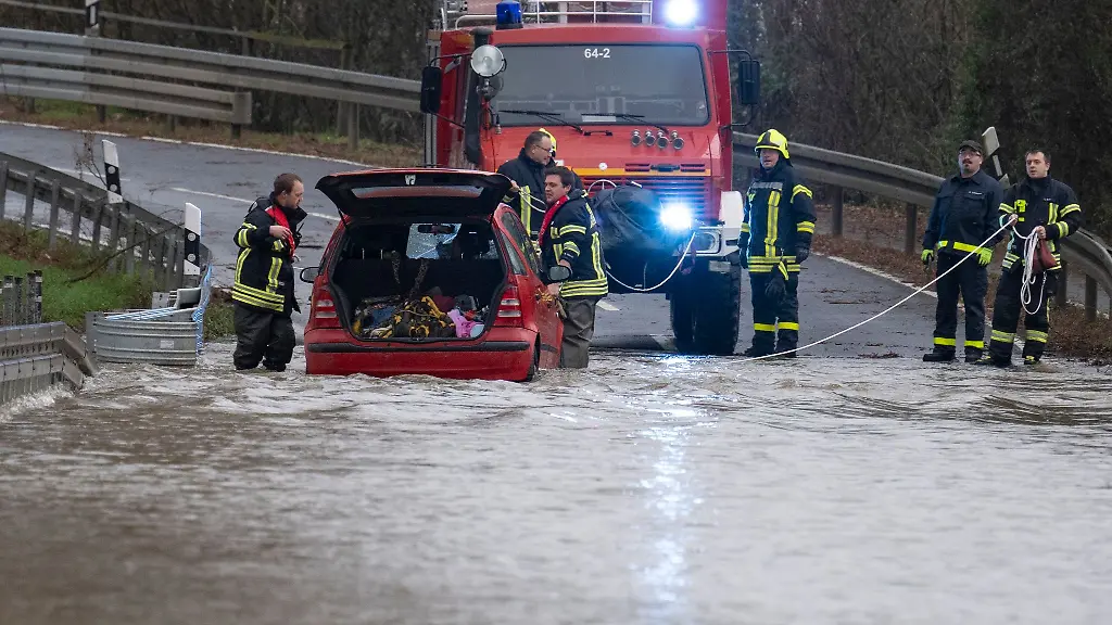 Feuerwehrleute-der-Freiwilligen-Feuerwehr-Heuchelheim-retten-eine-Frau-aus-ihrem-Fahrzeug-nachdem-diese-auf-einer-ueberfluteten-Landstrasse-im-Hochwasser-liegen-geblieben-war
