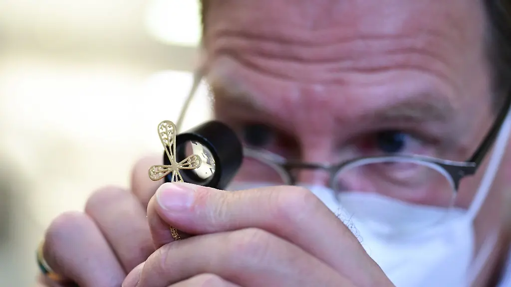 Ein-Mitarbeiter-einer-Pfandleihe-taxiert-ein-Kreuz-einer-Goldkette-mit-einer-Lupe