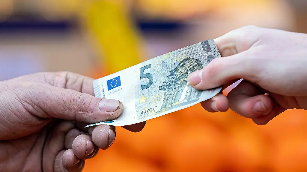 Ein-Kunde-bezahlt-seinen-Einkauf-an-einem-Stand-auf-einem-Wochenmarkt-mit-einem-Fuenf-Euro-Schein