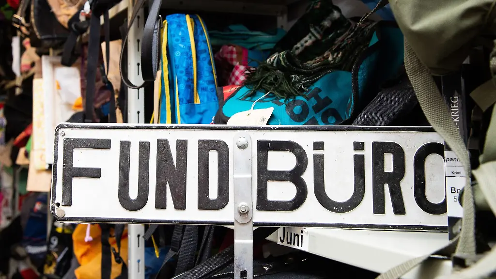 Ein-Schild-mit-der-Aufschrift-Fundbuero-steht-zwischen-Rucksaecken-und-Taschen-in-einem-Regal