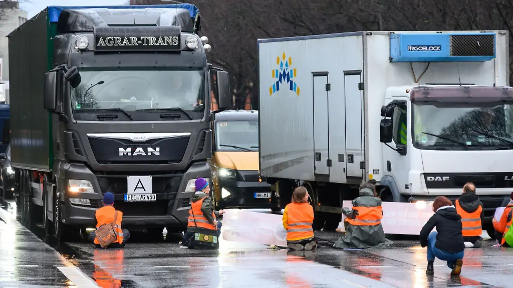 Aktivisten-sitzen-mit-teils-festgeklebten-Haenden-und-Plakaten-vor-im-Stau-stehenden-Fahrzeugen