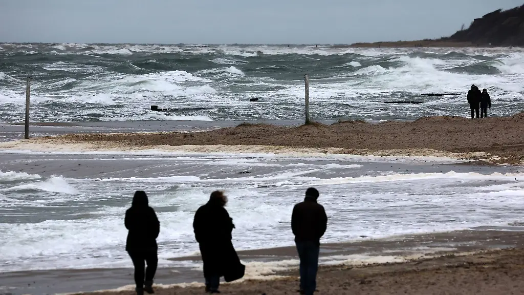 Spaziergaenger-sind-am-Ostseestrand-unterwegs-waehrend-der-stuermische-Wind-die-See-aufschaeumt