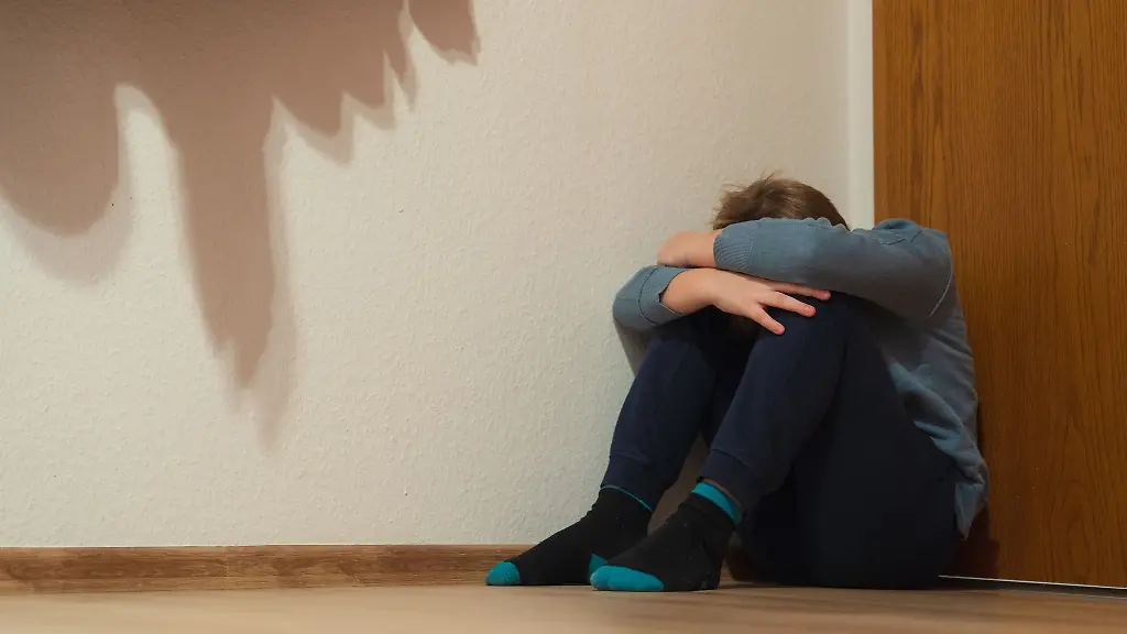 Ein-Junge-kauert-sich-in-der-Ecke-eines-Zimmers-am-Fussboden-sitzend-zusammen