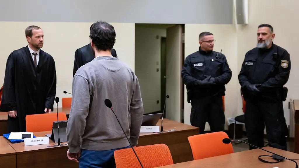 Der-Angeklagte-3-v-l-steht-zusammen-mit-Polizeibeamten-und-seinen-Anwaelten-Martin-Gelbricht-l-und-Maximilian-Baer-2-v-l-verdeckt-im-Verhandlungssaal