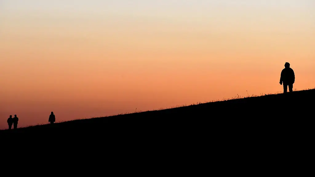 Spaziergaenger-gehen-beim-Sonnenuntergang-ueber-einen-Deich