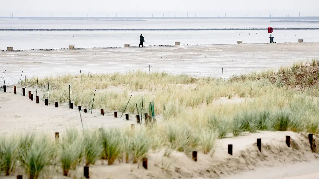 Eine-Urlauberin-geht-bei-regnerischem-Wetter-auf-einem-Weg-am-Strand-vor-der-Nordsee-entlang