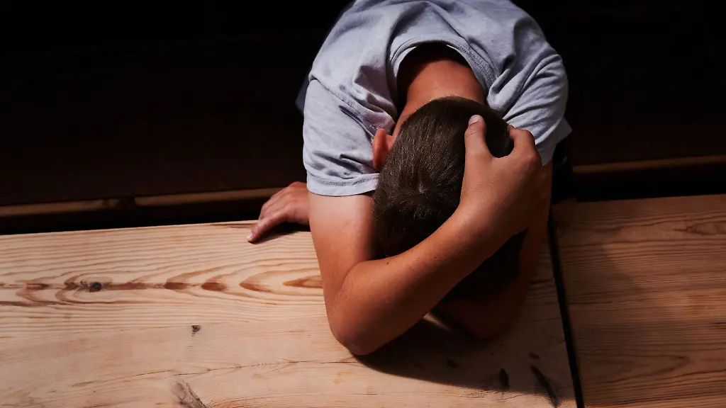 Ein-Kind-versteckt-sein-Gesicht-unter-seinen-Armen-und-liegt-mit-dem-Kopf-auf-einem-Tisch
