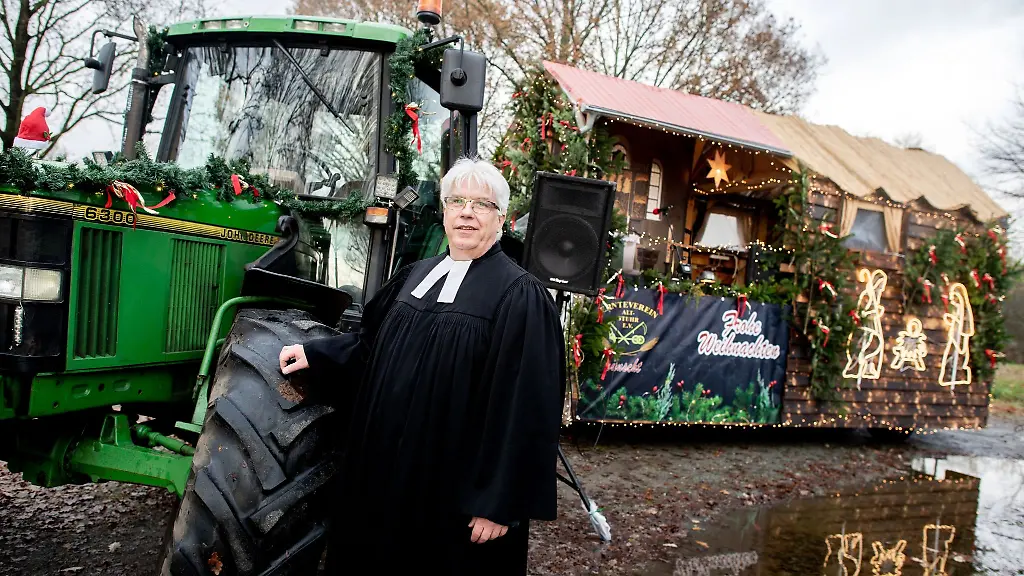 Pastor-der-evangelischen-Kirchengemeinde-Stuhr-Robert-Vetter-steht-vor-einem-Anhaenger-mit-Waldhuette-der-von-einem-Traktor-gezogen-wird