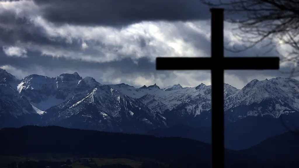 Wolkenverhangen-sind-die-schneebedeckten-Alpen-hinter-einem-Gipfelkreuz