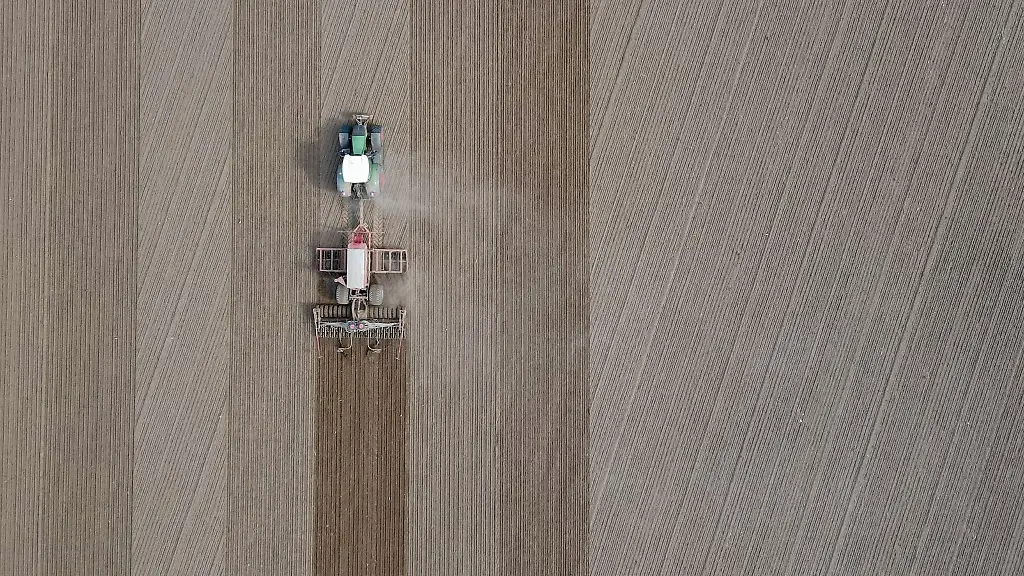 Ein-Landwirt-faehrt-mit-seinem-Traktor-und-angehaengter-Drille-ueber-ein-Feld