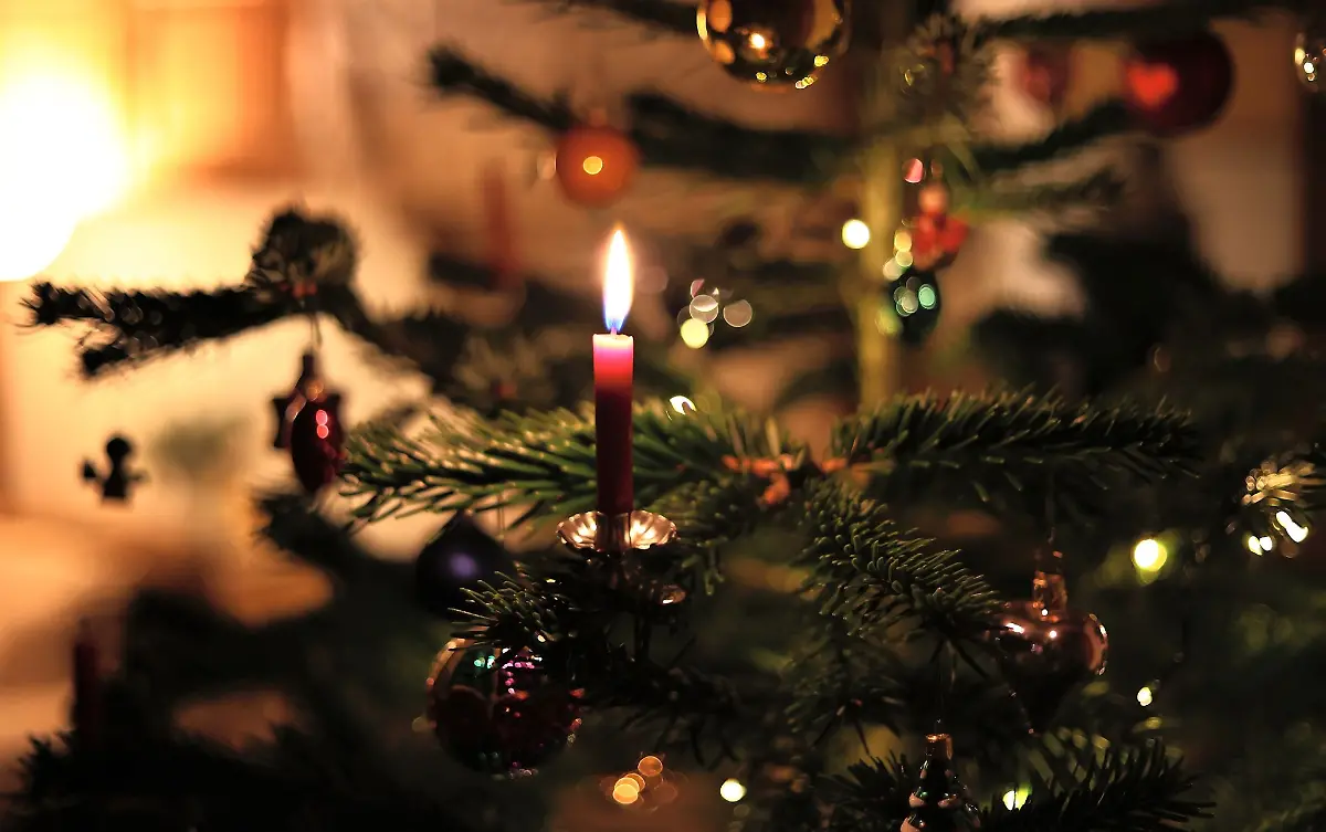 Eine-Kerze-brennt-an-einem-festlich-geschmueckten-Weihnachtsbaum