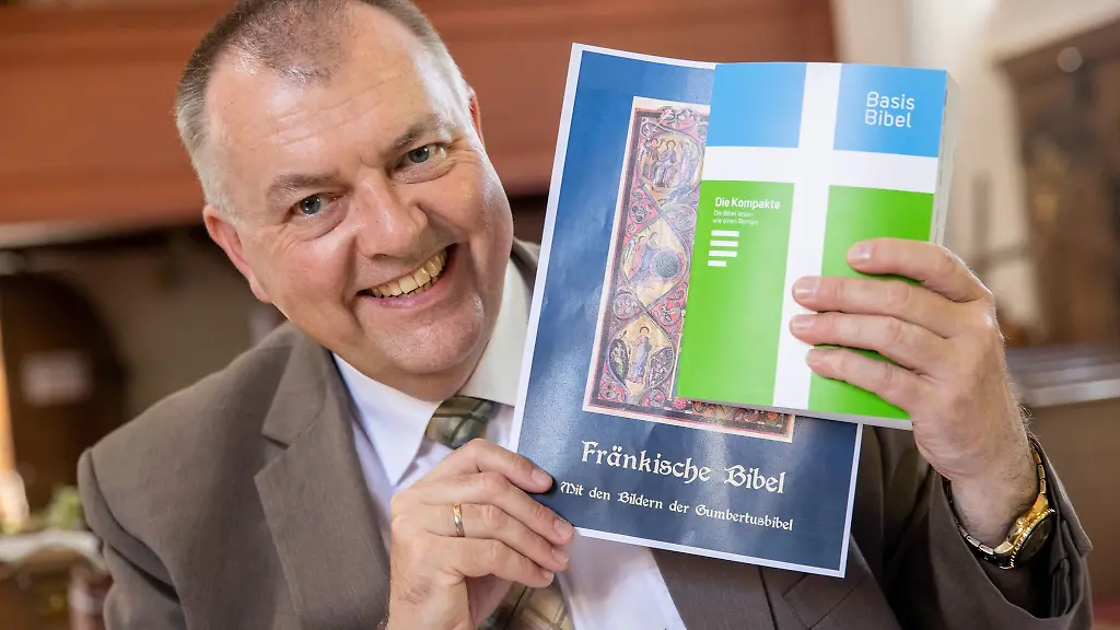 Pfarrer-Claus-Ebeling-haelt-einen-Entwurf-fuer-den-Buchdeckel-einer-Mundart-Bibel-neben-einer-herkoemmlichen-Bibel