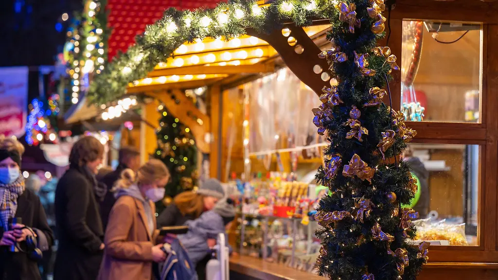 Besucher-eines-Weihnachtsmarktes-stehen-an-einem-Verkaufsstand-fuer-Suessigkeiten