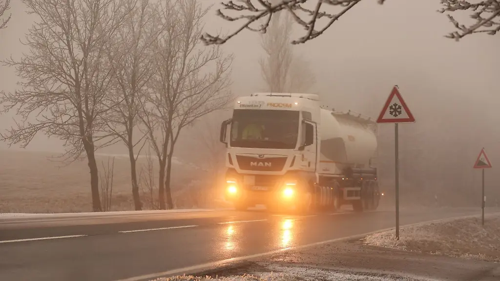 Ein-Lkw-faehrt-bei-Glatteis-und-Nebel-ueber-eine-Strasse