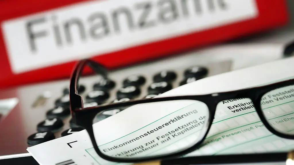 Auf-einem-Vordruck-fuer-die-Steuererklaerung-liegt-vor-dem-Aktenordner-mit-dem-Aufdruck-Finanzamt-ein-Stift-und-eine-Brille