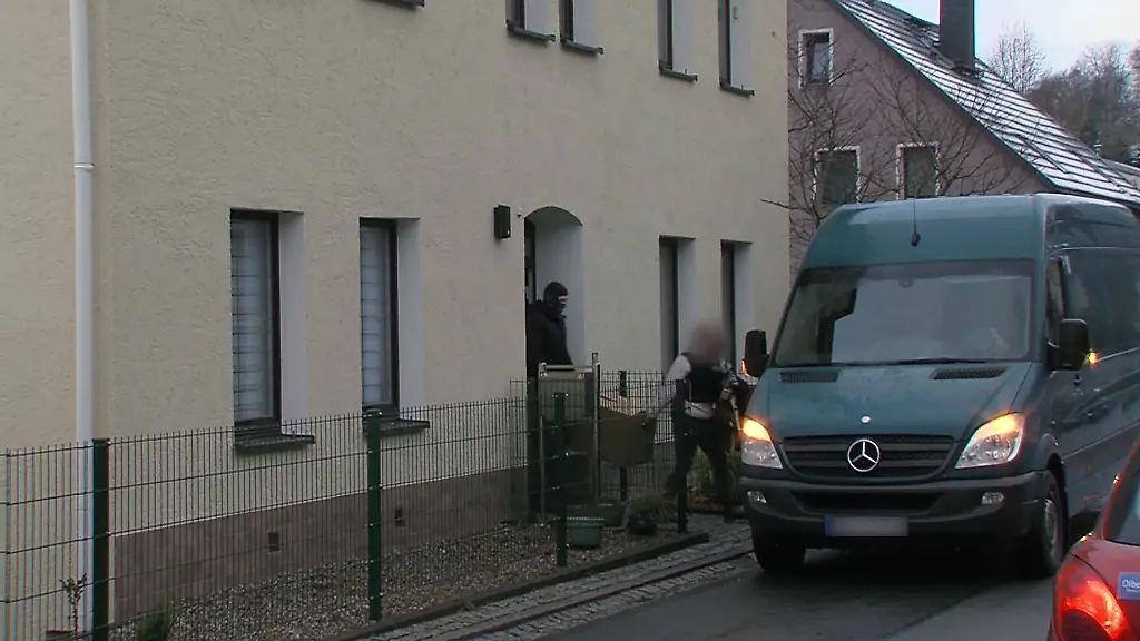 Polizisten-tragen-im-Rahmen-einer-Durchsuchung-einen-Karton-aus-einem-Wohnhaus