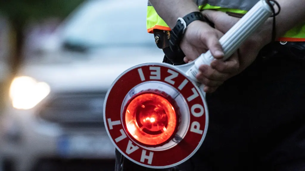 Ein-Polizist-haelt-bei-einer-Verkehrskontrolle-eine-Winkerkelle-in-der-Hand