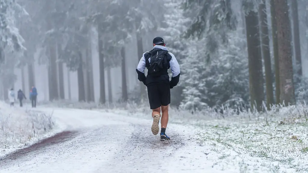 Ein-Trailrunner-laeuft-auf-einem-schneebedeckten-Waldweg-Richtung-Feldberggipfel