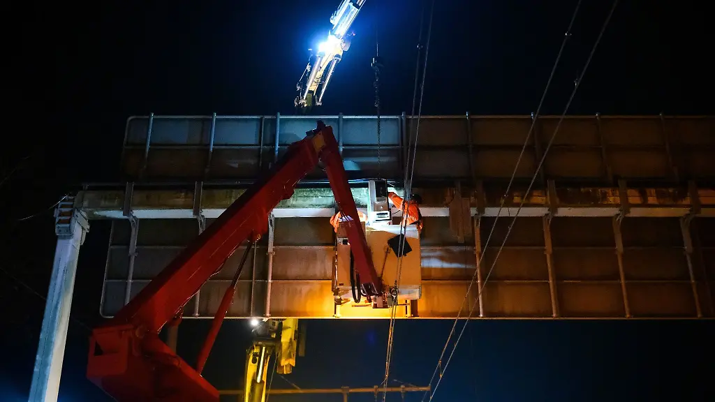 Zwei-Arbeiter-in-einem-Hubsteigerkorb-installieren-ein-Messgeraet-an-einer-Schilderbruecke-ueber-den-Stromleitungen