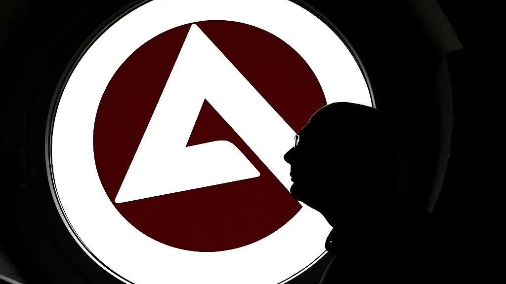 Ein-Mann-steht-in-der-Bundesagentur-fuer-Arbeit-vor-einem-Fenster-mit-dem-Logo-der-Agentur
