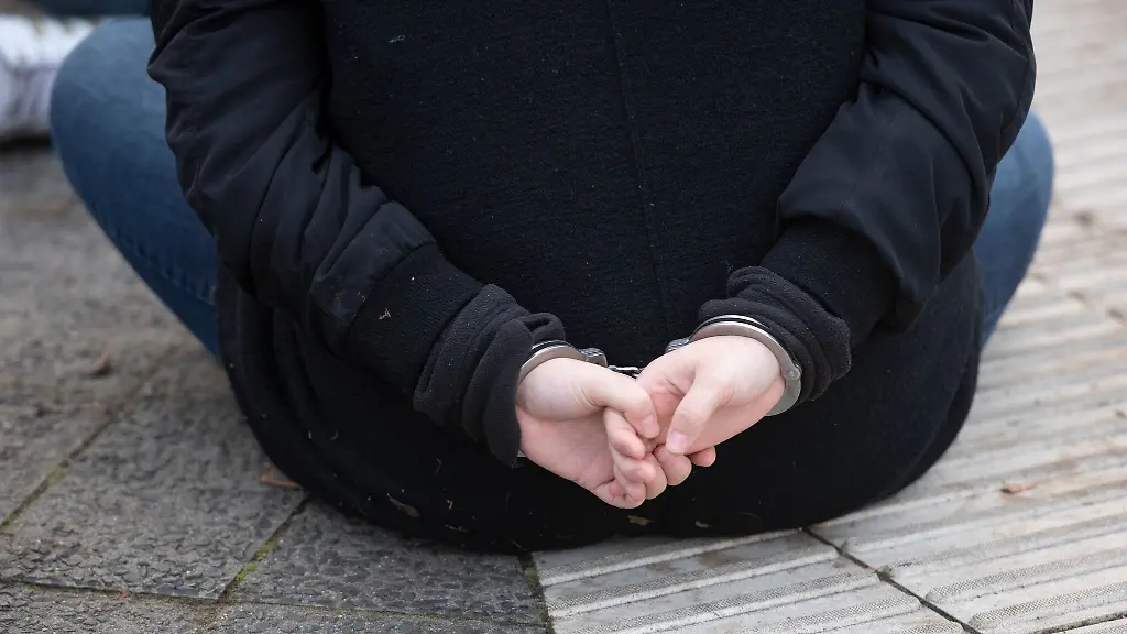 Eine-Aktivistin-der-Gruppe-Letzte-Generation-sitzt-mit-Handschellen-gefesselt-auf-einer-Strasse